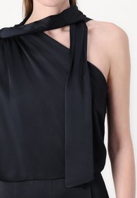 Top preto sem mangas em tecido leve, com um colarinho drapeado e um design de um ombro, apresentando uma textura suave e um corte elegante.