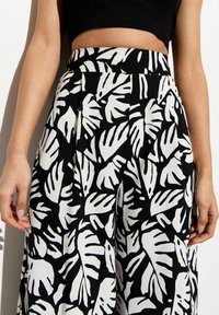 Pantalon large taille haute noir et blanc à imprimé feuilles tropicales audacieux, porté avec un haut court noir.