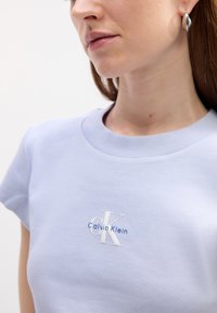 Jasnoniebieska koszulka z krótkim rękawem z żeberkowym dekoltem i wyszywanym logo "Calvin Klein" w białym i niebieskim kolorze na piersi.