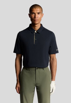 Marine polo med en detaljeret krave, tre knapper og en kontrasterende gul stribe. Sammen med olivengrønne bukser og en hvid handske.
