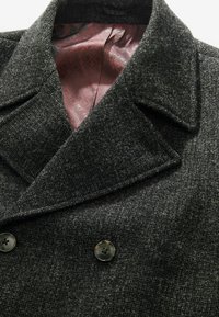 Abrigo gris texturizado con un frente de doble botonadura, que presenta grandes botones negros y un forro estampado en burdeos que contrasta.