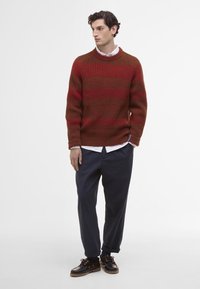 Roter und brauner, horizontal gestreifter Strickpullover, runder Ausschnitt, mit gerippten Bündchen und Saum. Über einem weißen Hemd mit Kragen und einer marineblauen Hose getragen.