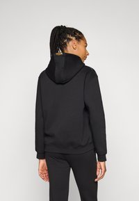 Hoodie preto feito de tecido macio, com um cordão ajustável e um logótipo nas costas. O design tem um corte descontraído e punhos com canelado.