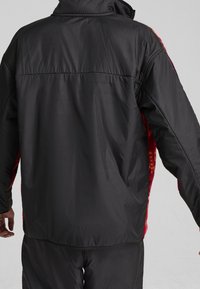 Black puffer jacket featuring a high collar, elastic cuffs, and red fleece accents on the sides. Smooth texture and loose fit.
