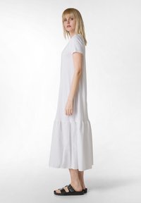 Vestido blanco hasta la rodilla, hecho de una tela suave, con mangas cortas y un dobladillo en capas. Combinado con sandalias negras con correas ajustables.