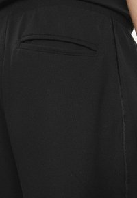 Joggers neri con tasca posteriore, trama liscia, cuciture pulite e design semplice senza loghi o motivi visibili.