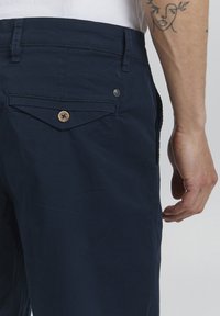 Marineblå bomullsbukser, detaljert med en baklomme med knappelukking og et lite logo-påbud, glatt tekstur, slim fit.