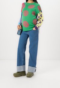 Pull tricoté vert vif avec des imprimés de fleurs roses, associé à un jean en denim bleu à jambes larges avec ourlet effiloché et des chaussures à plateforme vert olive.