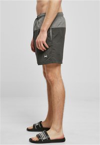 Schwarze und graue Badeshorts mit elastischem Bund und Kordelzug, mit einem kleinen Logo-Patch am unteren Bein.
