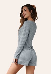 Set di abbigliamento comodo a coste grigio, composto da una maglia a maniche lunghe e pantaloni corti. Il tessuto è strutturato con una finitura morbida e una vestibilità rilassata.