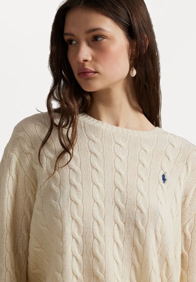Krem pulover z cable-knit vzorcem in okroglo ovratnikom ter modrim logotipom. Mehka tekstura ustvarja prijeten videz in sproščen silhuet.