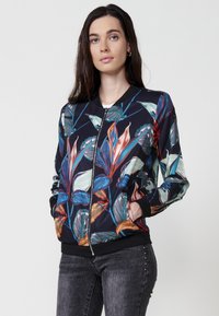 Giacca bomber con sfondo nero caratterizzata da un vivace motivo floreale tropicale nei toni del blu, arancione e verde. Polsini a costine e chiusura con zip.