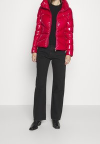 Röd puffjacka med glansig yta, dragkedjestängning och huva; bärs över en svart topp och matchas med svarta utsvängda byxor och svarta stövlar.