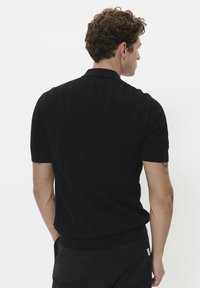 Black short-sleeve polo shirt with textured knit fabric, a collar, and a slim fit. Features ribbed cuffs and hem, with subtle branding on the side.