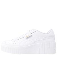 Baskets à plateforme blanches avec une tige en cuir lisse, embout perforé, lacets plats et semelle en caoutchouc texturée. Détail logo doré sur le côté.