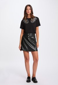 Zwarte T-shirt met korte mouwen met bloemendecoraties bij de hals, gecombineerd met een hooggesneden zwarte leren rok met dubbele gespen.