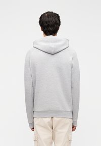 Γκρι φούτερ με κουκούλα, υφή στο ύφασμα, κορδόνι στην κουκούλα και ριμπ μανσέτες. Η πλάτη είναι λεία με τελείωμα που βρίσκεται πάνω από τη μέση.