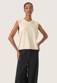 Top sans manches beige en tissu doux, doté d'un col rond et d'une coupe décontractée, associé à un pantalon noir à jambes larges.