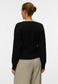 Must_fw knit-sweater ümmarguse kaelusega ja pikkade varrukatega, millel on lõdva istuvuse ja soonikkoes äär, kombineeritud heleda beeži püksiga.