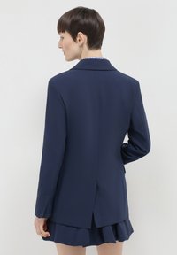 Blazer navy con un design su misura, apertura singola sul retro, maniche lunghe e colletto a falde, abbinato a una gonna a strati.