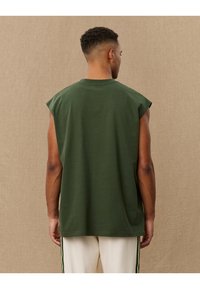 Zöld ujjatlan pamut póló, kerek nyakkivágással és laza szabással. Sima textúra és minimalista design.