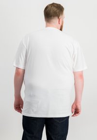 T-shirt bianca a maniche corte con colletto rotondo, realizzata in cotone. Texture liscia e design semplice, infilata in un paio di jeans blu scuri.