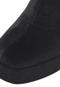 Chaussure en tissu noir avec une texture lisse, une forme incurvée et une semelle contrastante. Des détails de couture sont visibles le long des côtés et des orteils.