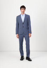 Hellblaues Anzug mit spitzem Revers, Ein-Knopf-Verschluss und zwei Fronttaschen; kombiniert mit einem hellblauen Hemd mit Kragen und schwarzen Schuhen.