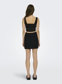 Zwarte crop top met vierkante halslijn, voorzien van een oogjespatroon. Bijpassende strakke mini-jurk met een vergelijkbaar ontwerp. Model draagt zwarte platform schoenen.