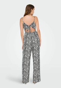 Jumpsuit de patrón en blanco y negro con tirantes finos, espalda abierta con detalle de nudo, pantalones de pierna ancha y cintura elástica.
