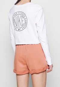 Vit långärmad croppad skjorta med en svart cirkulär logotyp på ryggen. Matchad med persikofärgade, mjuka shorts med rullad fåll.