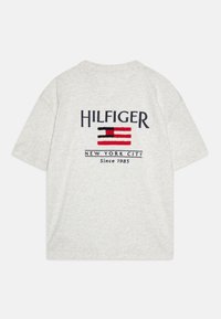 Lys grå kortærmet t-shirt med navy og rød broderet "HILFIGER" logo og "NEW YORK CITY Siden 1985" tekst på ryggen.