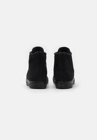 Černé semišové kotníkové tenisky s texturovanou látkou, pryžovými podrážkami a vyraženými značkovými detaily na zadní straně. Bez viditelných tkaniček.