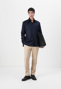 Camică bleumarin cu mânecă lungă, pantaloni bej, pantofi negri și o geantă de umăr neagră. Textură fină, croială clasică și design minimalist.