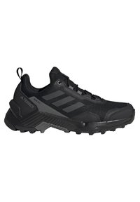 Chaussure de trail Adidas Terrex noire avec semelle robuste, tige en mesh, languette à l’arrière et trois bandes foncées sur le côté.