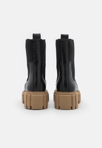Bottines en cuir noir avec semelles épaisses marron rainurées, languettes arrière et panneaux latéraux élastiques montrées de dos.
