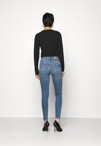 Top negro de manga larga, vaqueros ajustados azul claro y tacones altos negros. Los vaqueros tienen bolsillos traseros y una etiqueta en la cintura. Textura suave.