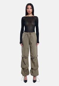 Zwart lang mouwtopje met golfpatroon, gecombineerd met gestructureerde kaki broek met trekkoord taille en gelaagd ontwerp. Zwarte schoenen met hoge hak.