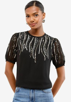 Schwarzes Shirt mit Puffärmeln, verziert mit silbernen Pailletten in einem kaskadierenden Muster. Weicher Stoff mit glatter Textur, lässige Passform.