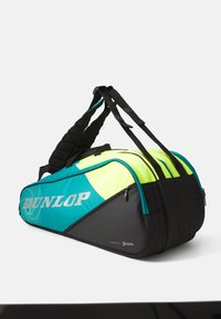 Dunlop sporto krepšys su juodu pagrindu, ryškiai geltonomis ir turkio spalvos detalėmis, paminkštintu diržu ir užtrauktuku uždaru skyriumi saugiam daiktų laikymui.