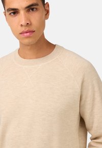 Svetlo bež majica s crewneck izrezom s teksturiranim finišem. Ima raglan rukave i rebrasti izrez. Enostaven, brez okrasitev dizajn.