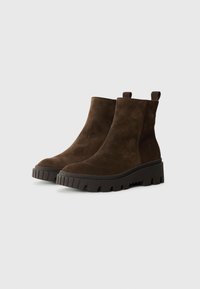 Brune ruskinds ankelstøvler med en chunky sort gummisål, der har et strukturelt mønster, og løfteløkker bagpå for nem påtagning.