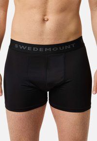 Czarne bokserki o gładkiej fakturze i elastycznym pasie z napisem marki "SWEDEMOUNT" w szarych literach. Dopasowany fason.