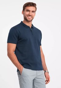 Granatowa koszulka polo wykonana z mieszanki bawełny, z krótkim zamkiem błyskawicznym i krótkimi rękawami, zestawiona z jasnoszarymi spodniami.