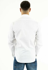 Chemise blanche à manches longues avec un col boutonné, texture lisse et léger éclat, associée à un jean en denim bleu.