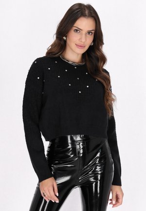 Maglione corto nero con lavorazione a maglia testurizzata e accenti di strass sparsi, abbinato a pantaloni in vinile nero lucido, caratterizzati da una silhouette aderente.