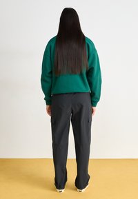 Groene oversized sweatshirt met drop schouders, gecombineerd met zwarte cargo broeken met zijzakken. Lange rechte haren zichtbaar.