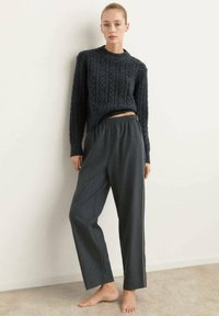 Maglione scuro a maglia con un motivo testurizzato; pantaloni larghi grigi scuri con vita elastica e dettaglio a striscia laterale.