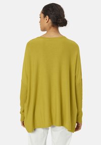 Pull ample à manches longues en tricot de couleur vert olive avec une texture côtelée et des épaules tombantes. L'ourlet est arrondi avec des fentes sur les côtés.