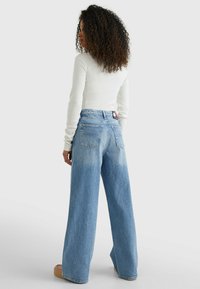Jeans de pierna ancha de color azul claro, confeccionados en denim con un lavado desgastado, que cuentan con bolsillos traseros y una etiqueta de marca en la cintura.